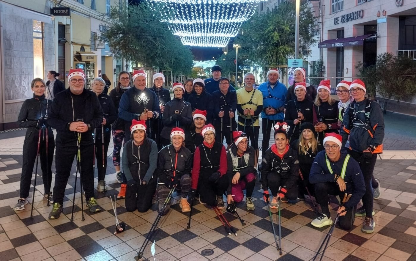 Photo de groupe du club de marche nordique Hyères Marche Nordique en bonnets de Noël, bâtons à la main, lors d'une sortie de Noël en soirée sous les illuminations de la ville, club de sport dans le Var.